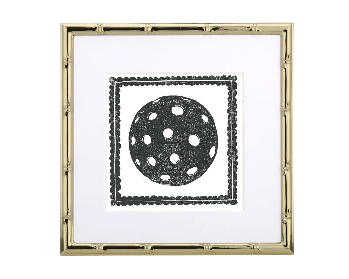 Decorative wall art with a black polka dot pickleball inside a gold frame on a white background