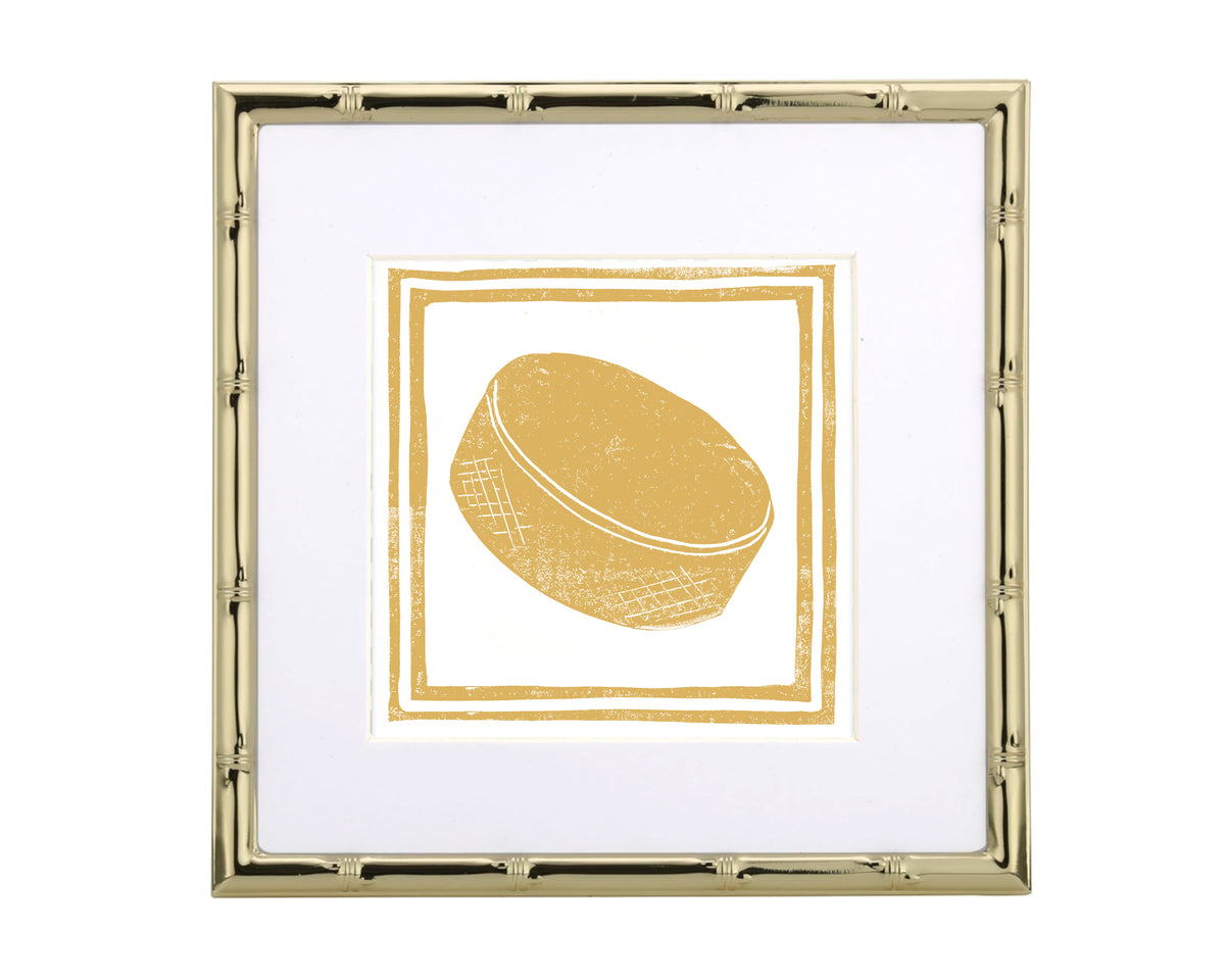 Framed artwork of a gold-colored hockey puck on a white background