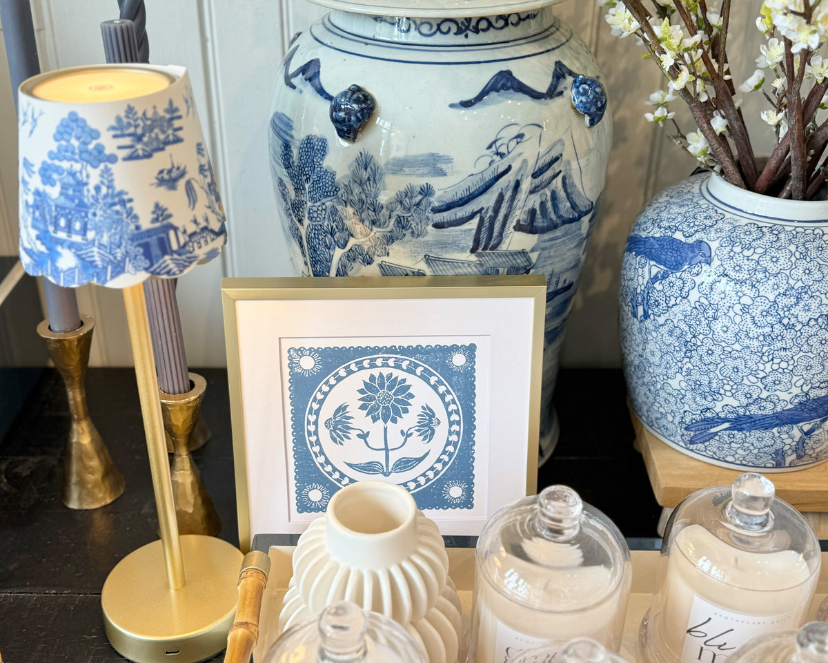 Decorative setting with blue and white ceramic vases, a lamp, and framed artwork on a dark surface.