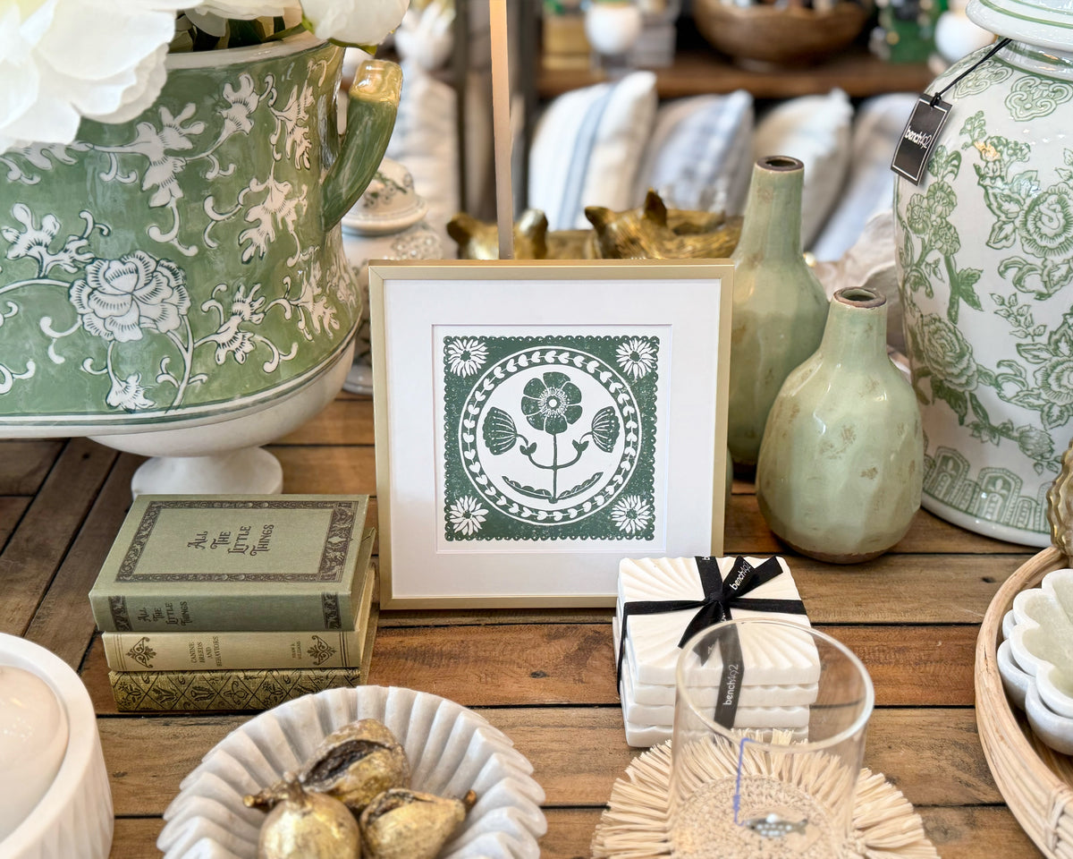 Decorative setting with green and white ceramic items, books, and a framed print on a wooden surface.