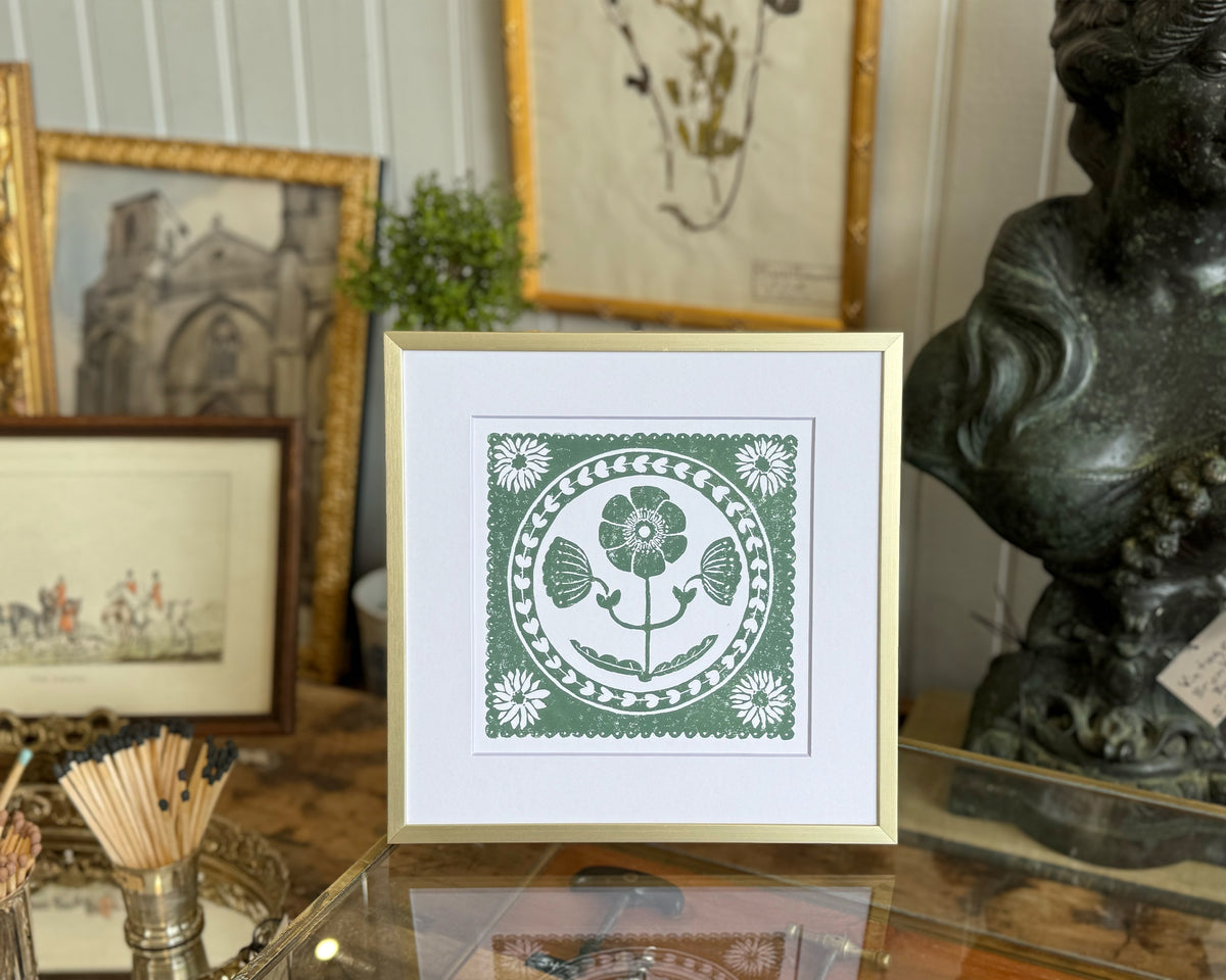 Framed artwork with a floral design on a table with decorative items.
