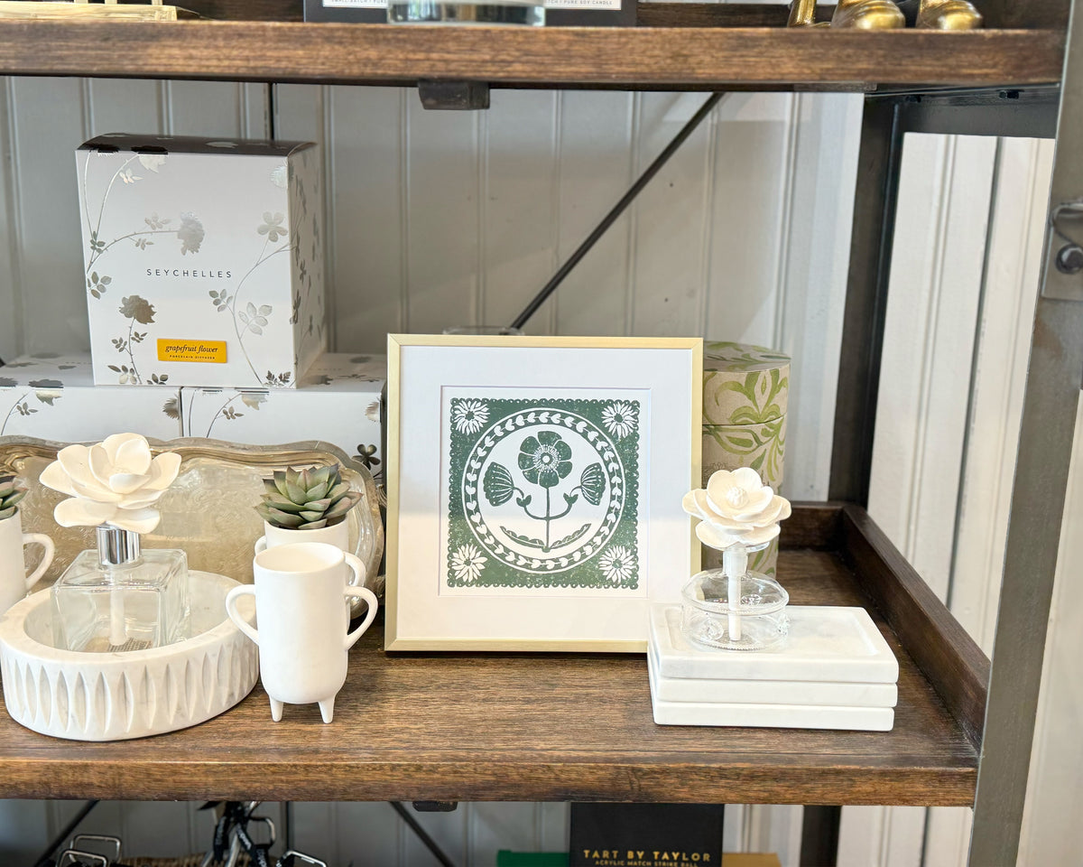 Decorative items on a wooden shelf including a framed print, cups, and small plants.