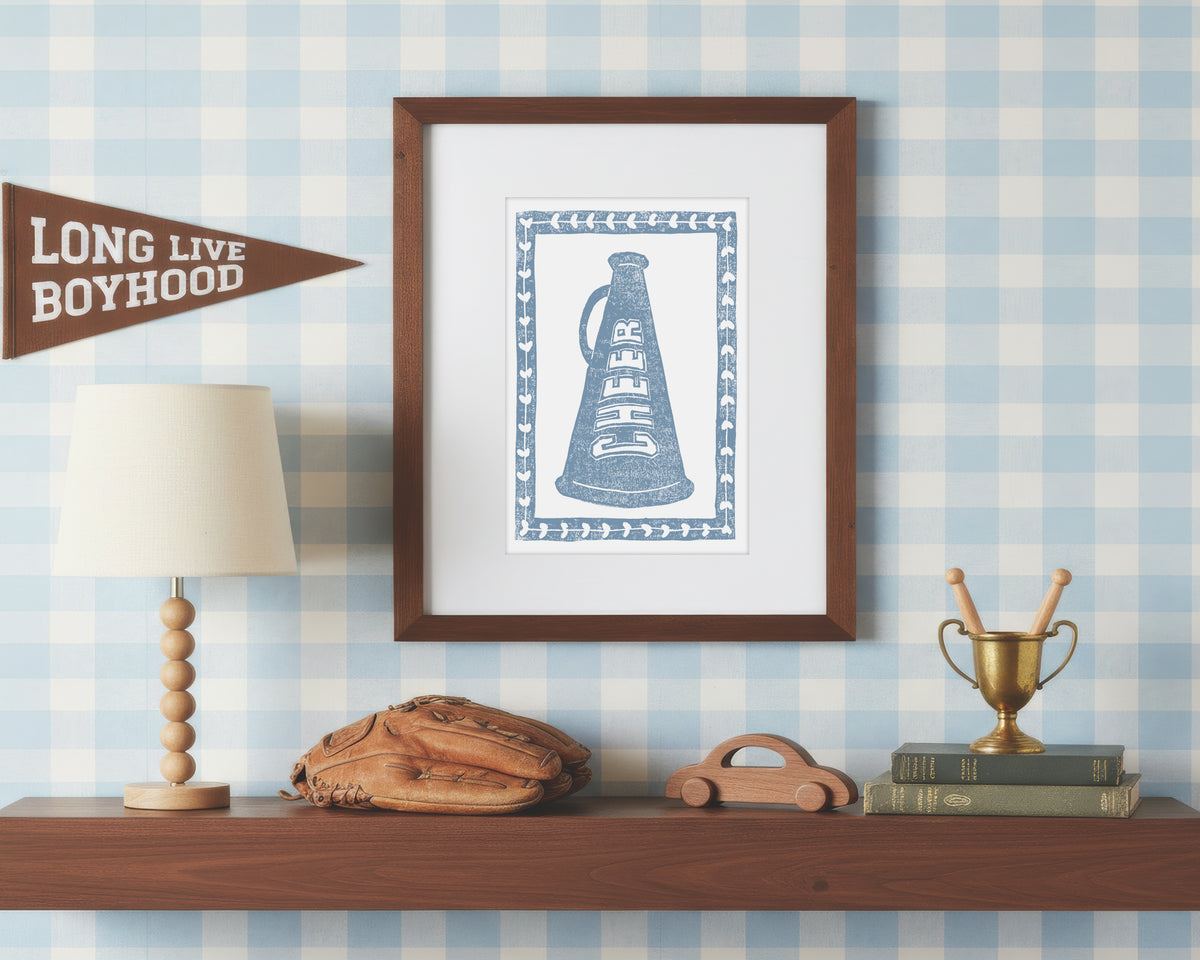 a framed art print of crossed cornflower blue cheerleading megaphone on a styled shelf in a blue and white bedroom