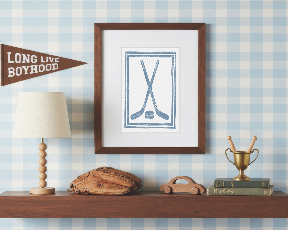 a framed art print of crossed cornflower blue hockey sticks and puck on a styled shelf in a blue and white bedroom