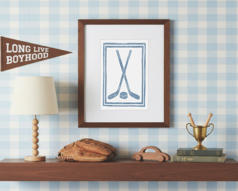 a framed art print of crossed cornflower blue hockey sticks and puck on a styled shelf in a blue and white bedroom