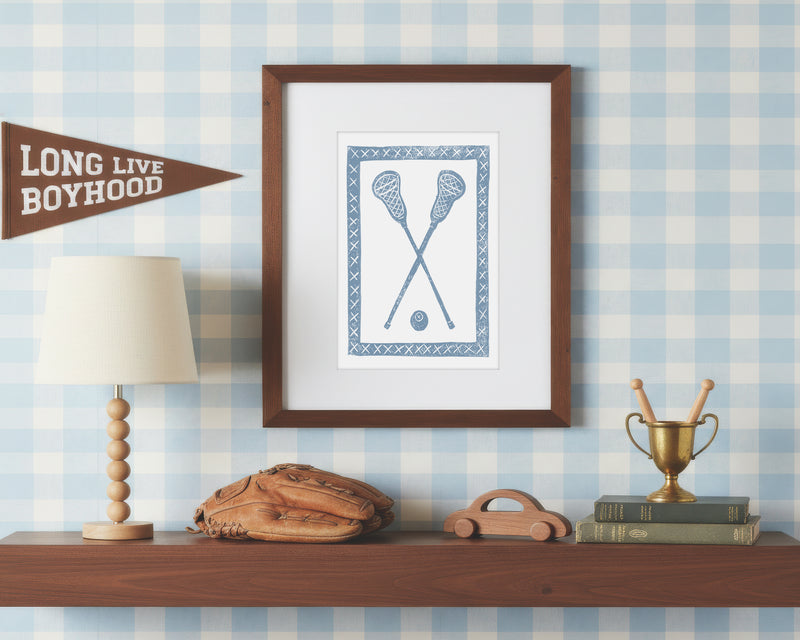 a framed art print of crossed cornflower blue lacrosse crosses and ball on a styled shelf in a blue and white bedroom
