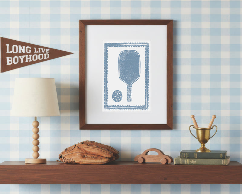 a framed art print of a cornflower blue pickleball racket and ball on a styled shelf in a blue and white bedroom