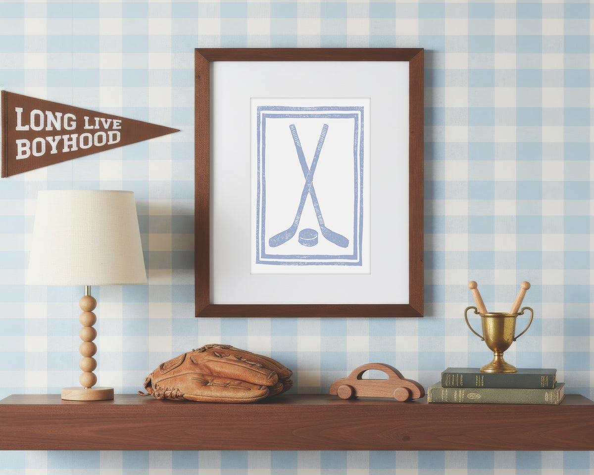 a framed art print of crossed light blue hockey sticks and puck on a styled shelf in a blue and white bedroom