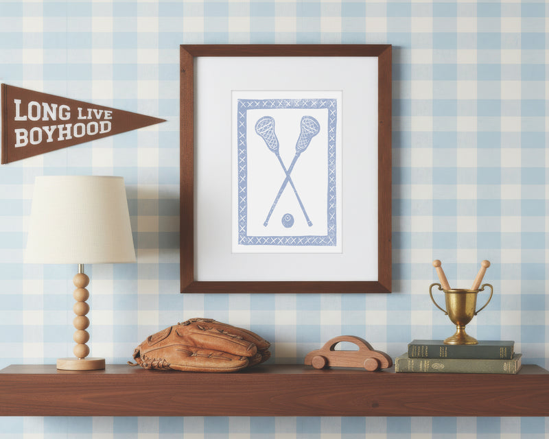 a framed art print of crossed light blue lacrosse crosses and ball on a styled shelf in a blue and white bedroom