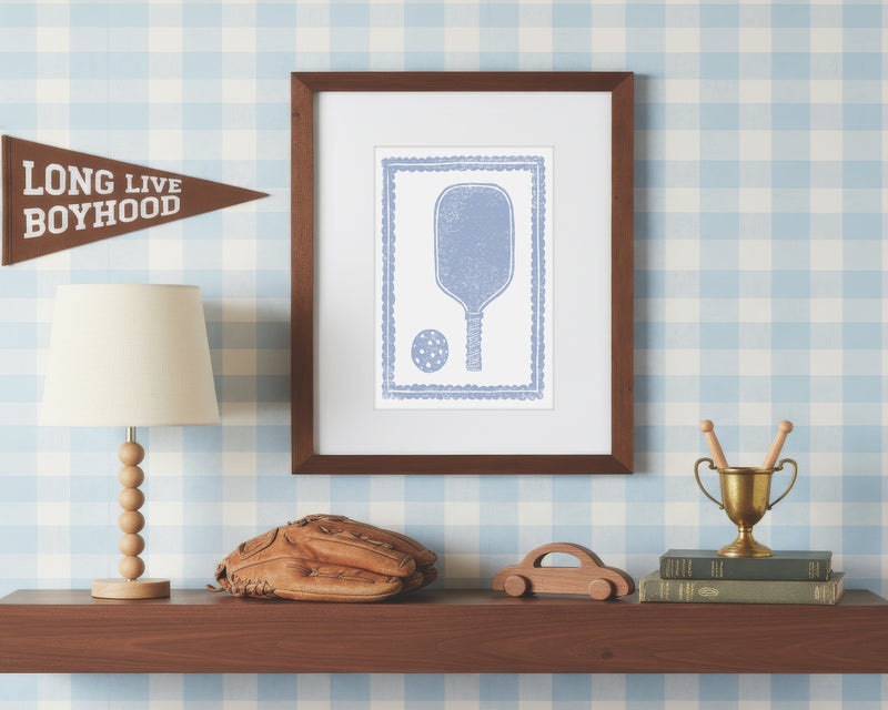 a framed art print of a light blue pickleball racket and ball on a styled shelf in a blue and white bedroom