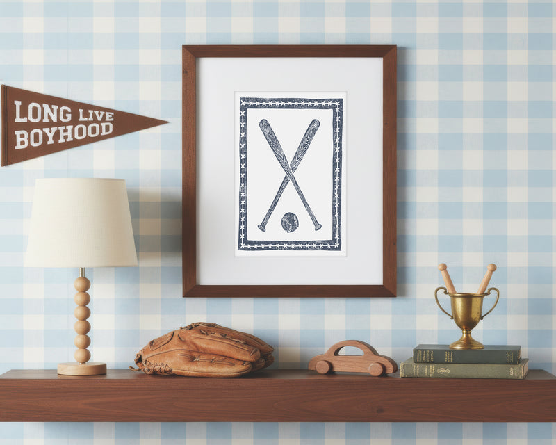 a framed art print of crossed navy blue baseball bats and ball on a styled shelf in a blue and white bedroom
