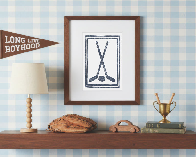 a framed art print of crossed navy blue hockey sticks and ball on a styled shelf in a blue and white bedroom