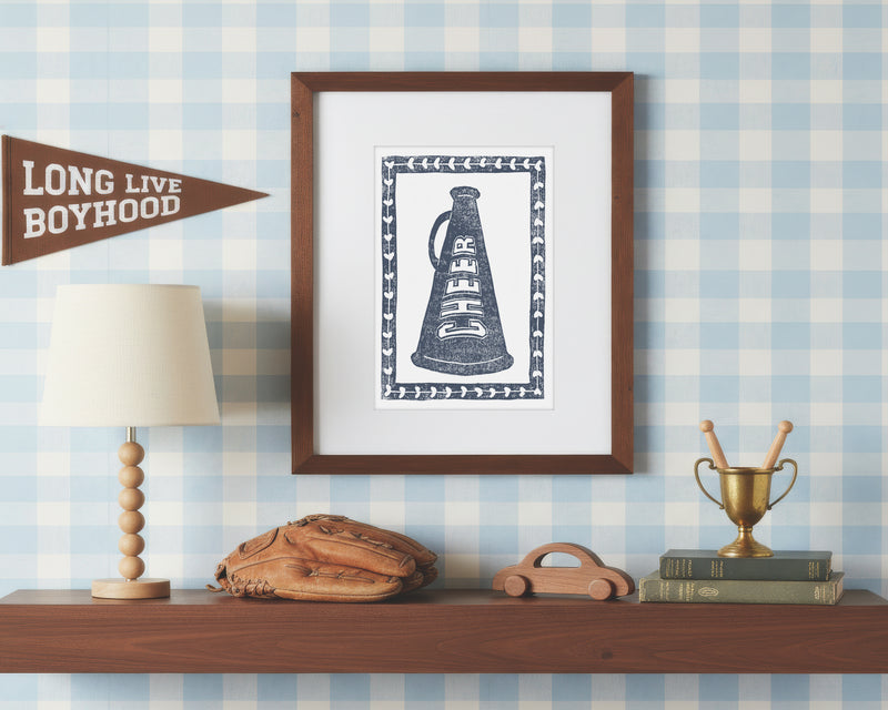 Framed print of a navy blue cheerleading megaphone on a wall with decorative items below.