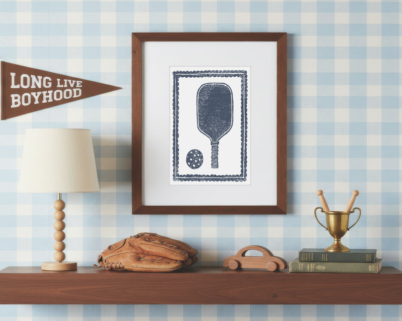 a framed art print of a navy blue pickleball racket and ball on a styled shelf in a blue and white bedroom
