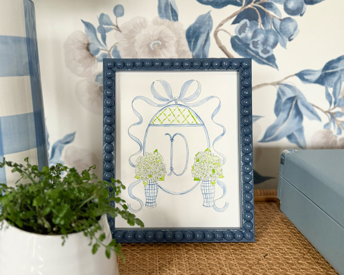 Decorative framed print with a blue frame on a wall with floral wallpaper.