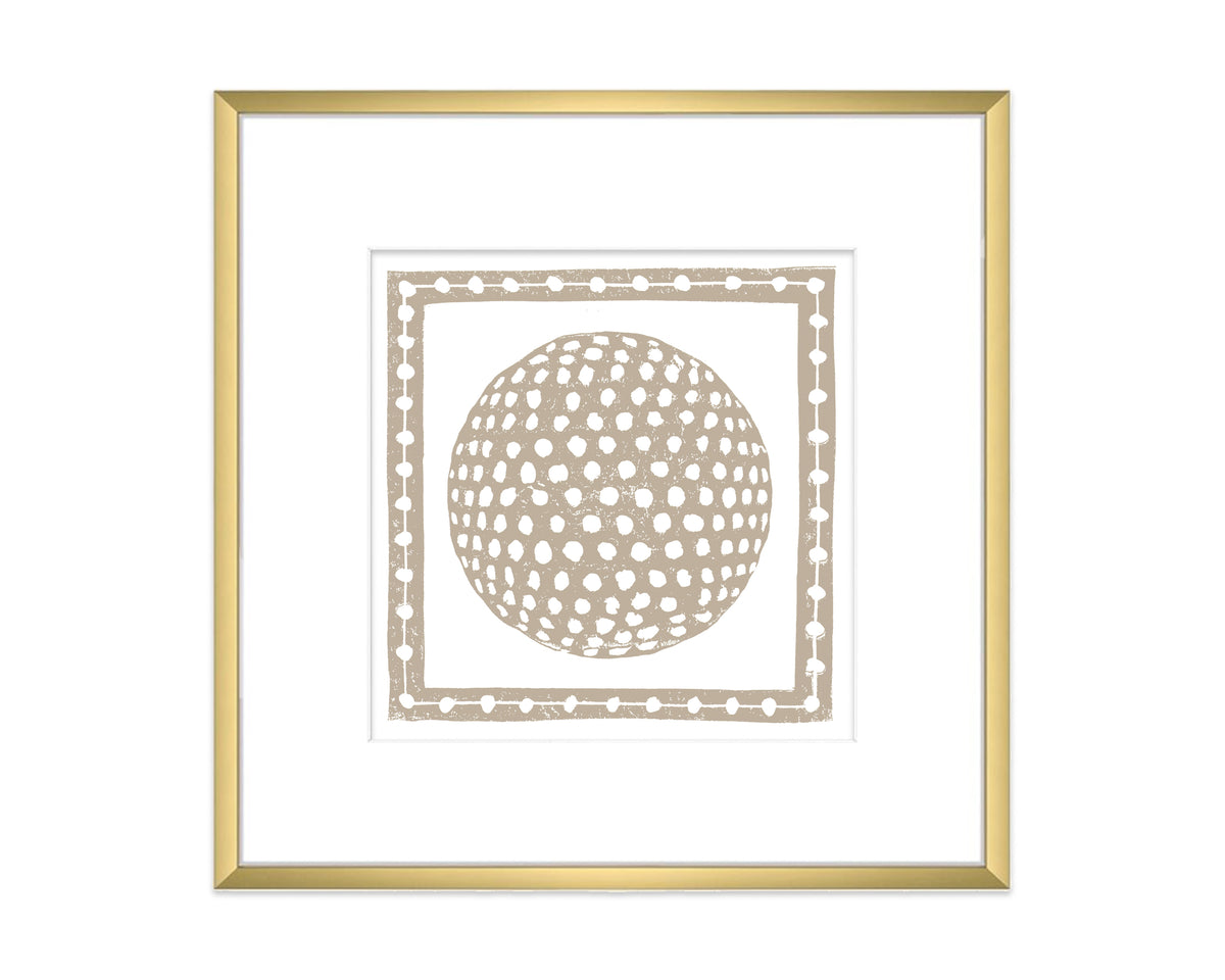 a tan golf ball in a decorative border and gold matted frame