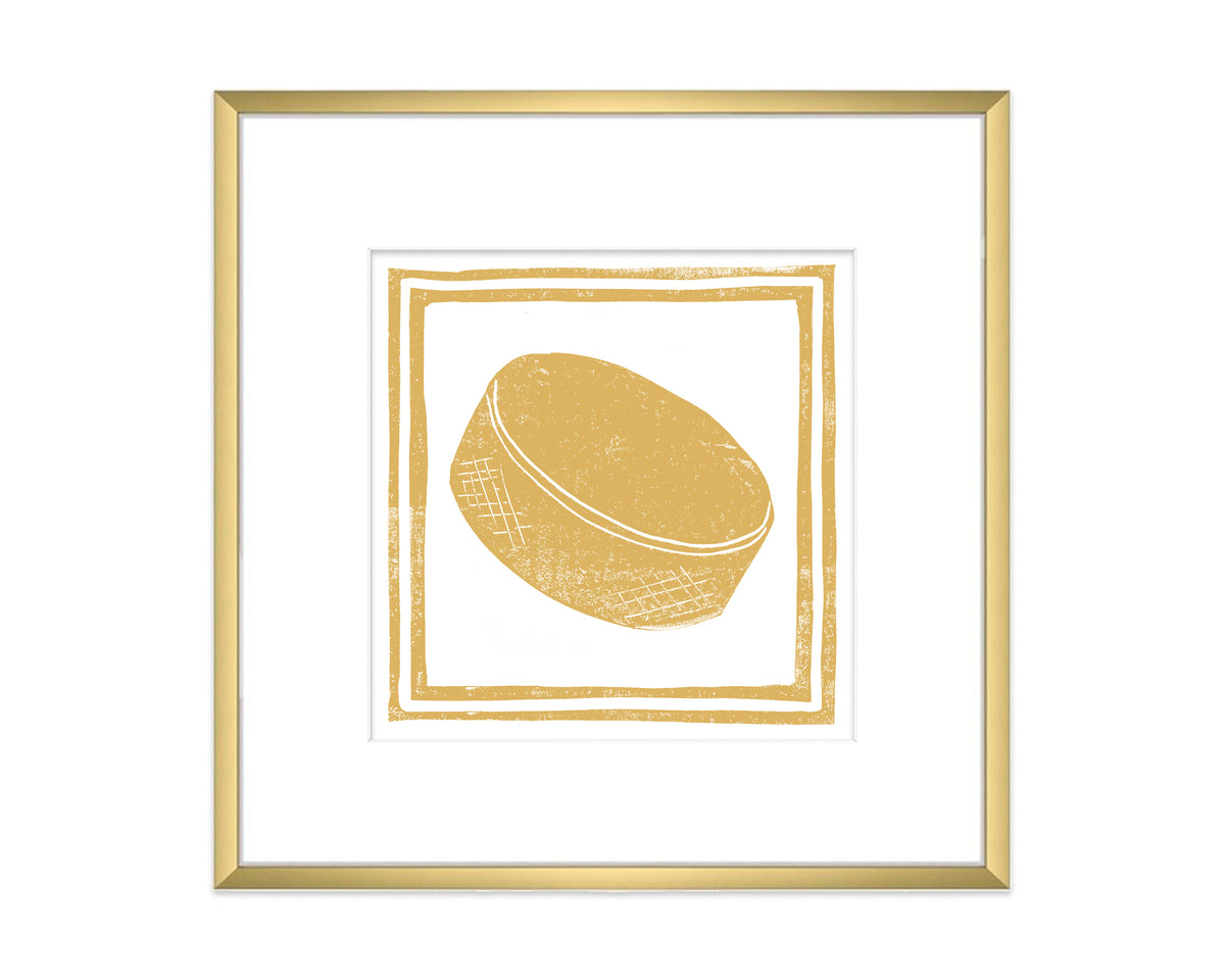 Framed artwork of a gold-colored hockey puck on a white background