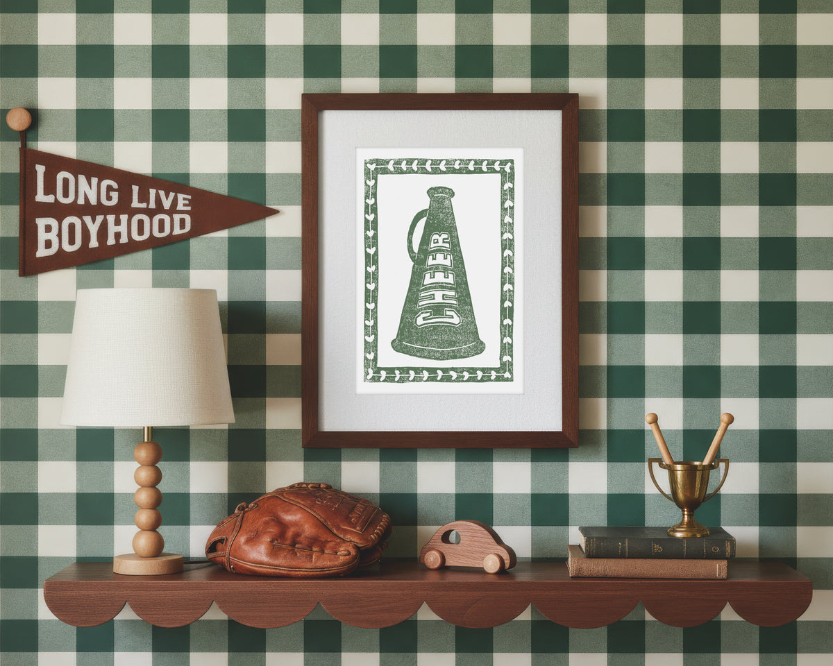A framed art print of a green cheer megaphone in a styled green and white bedroom