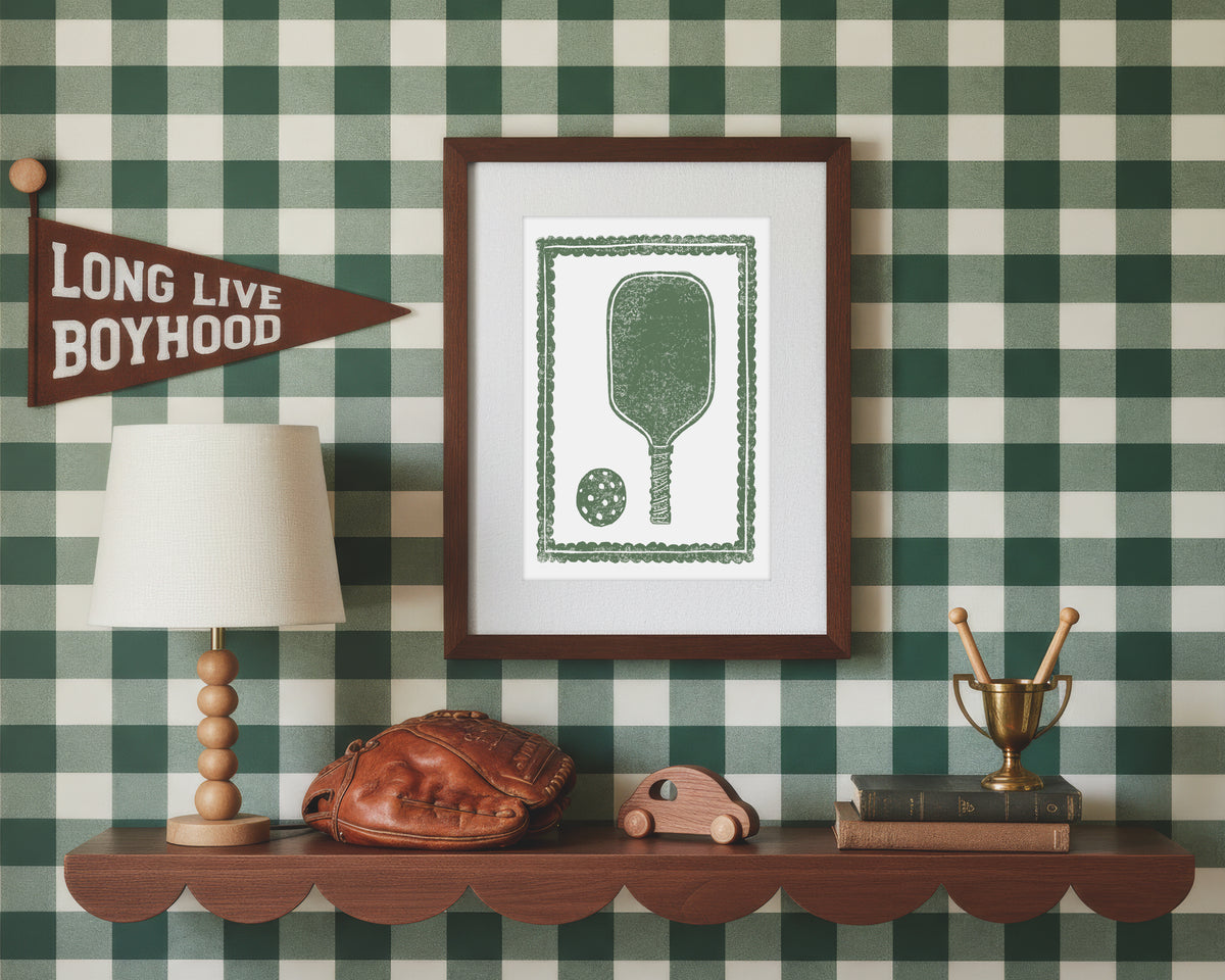 A framed art print of a green pickleball racket and ball in a styled green and white bedroom