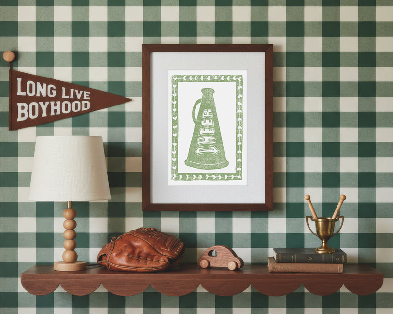 A framed art print of a sage green cheer megaphone in a styled green and white bedroom