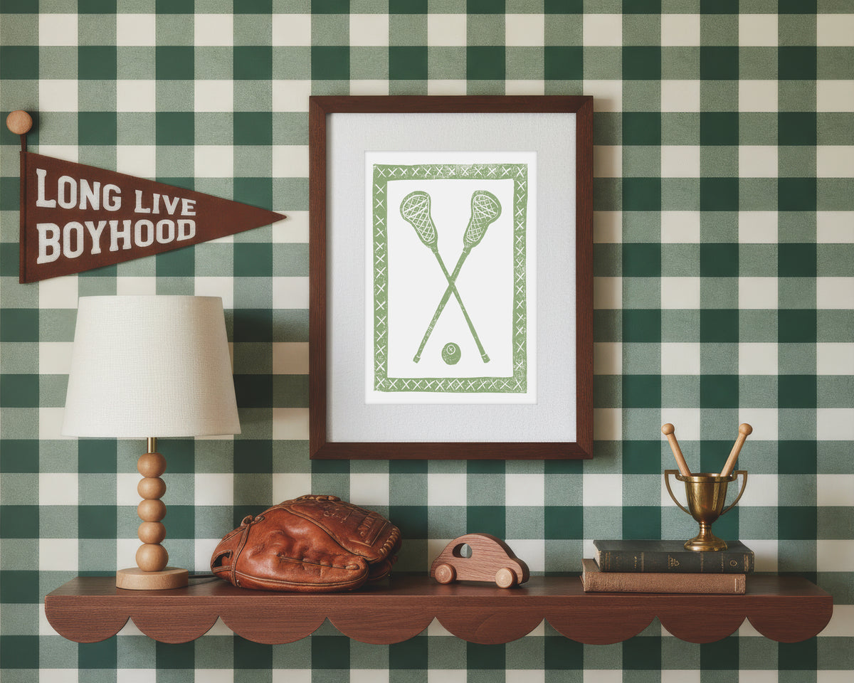 A framed art print of crossed green lacrosse crosses and ball in a styled green and white bedroom