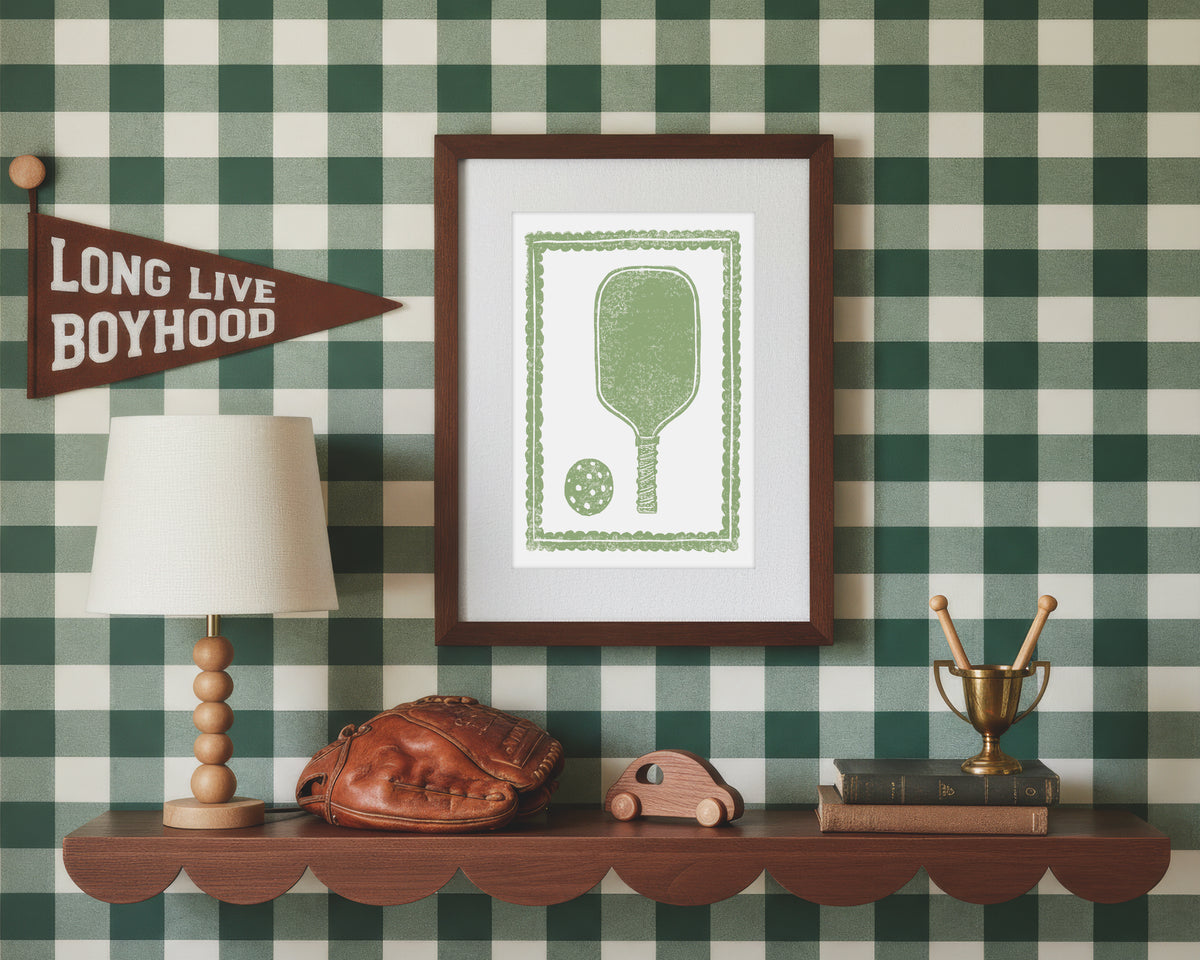 A framed art print of a sage green pickleball racket and ball in a styled green and white bedroom