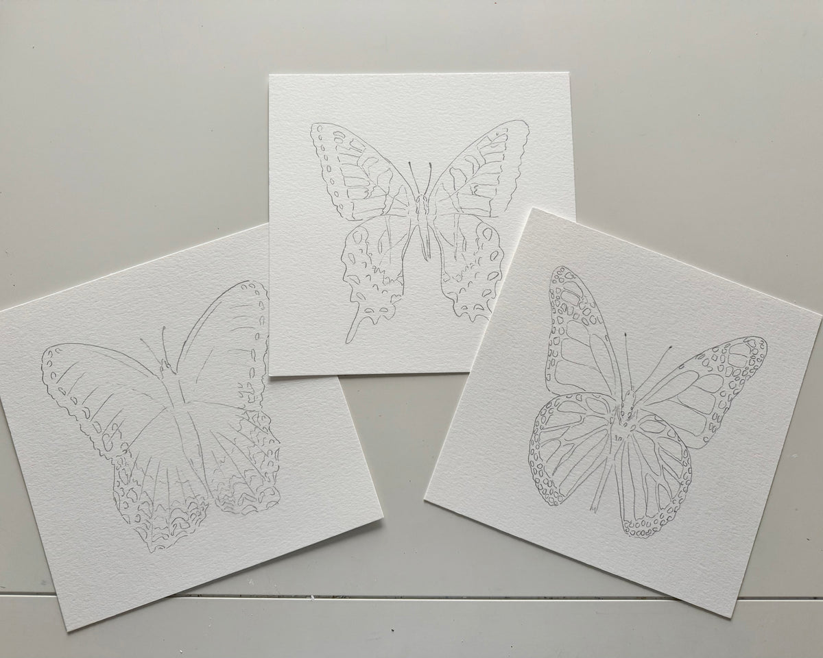 Three white cards with butterfly designs on a gray surface