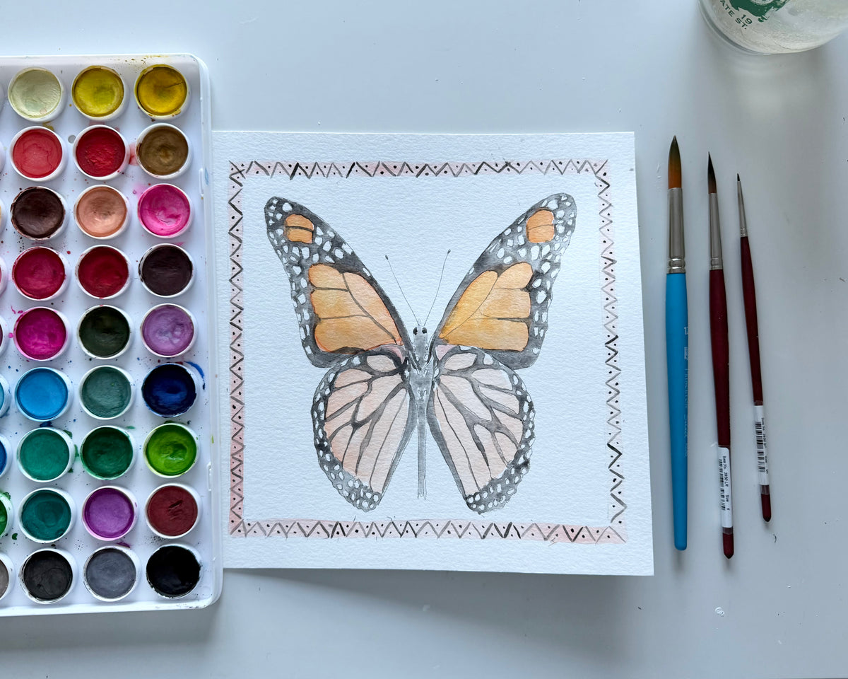 Butterfly drawing on paper with watercolor set and brushes on a light background