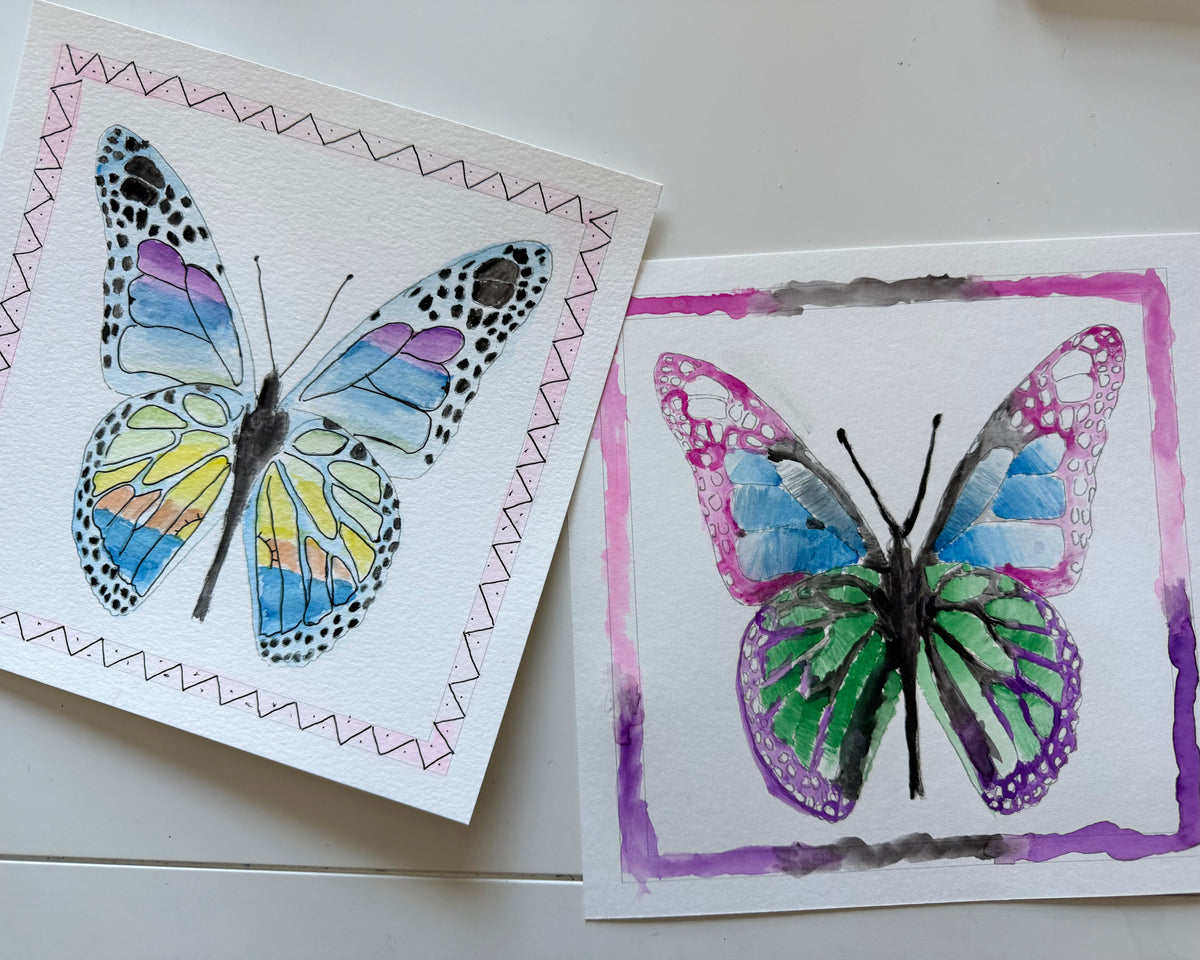 Two cards with watercolor butterfly designs on a white surface.