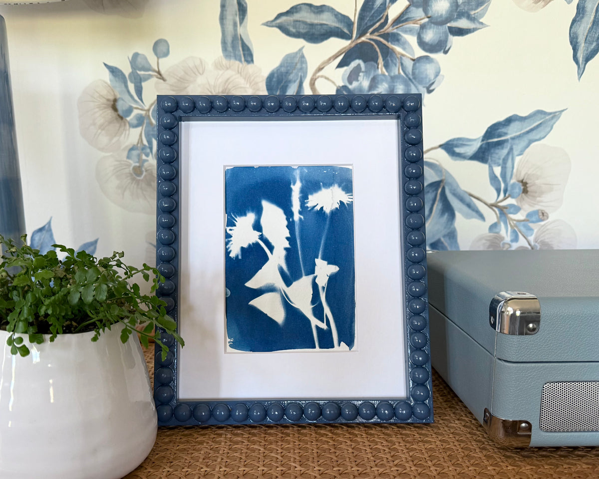 A framed blue and white cyanotype design in a frame on a styled desk
