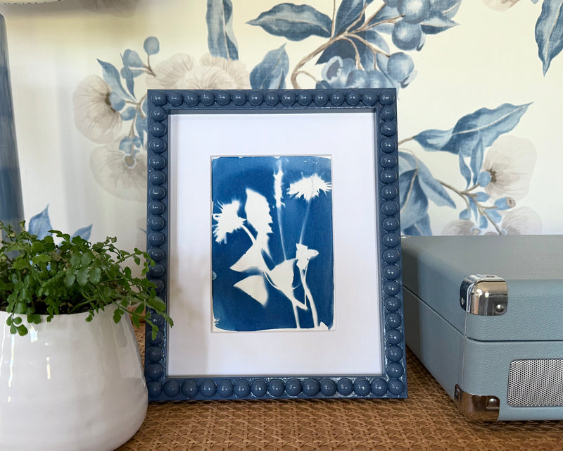 A framed blue and white cyanotype design in a frame on a styled desk