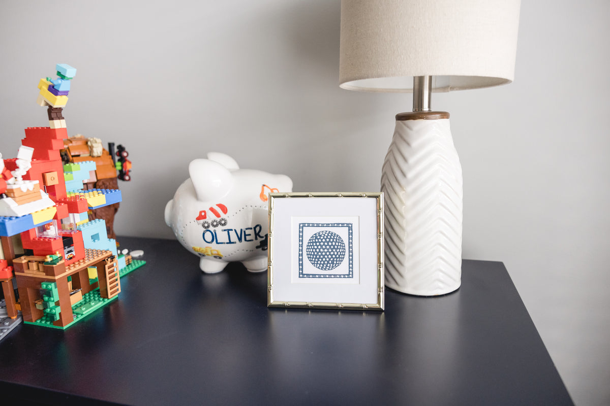 A framed blue golf ball print on a styled desk