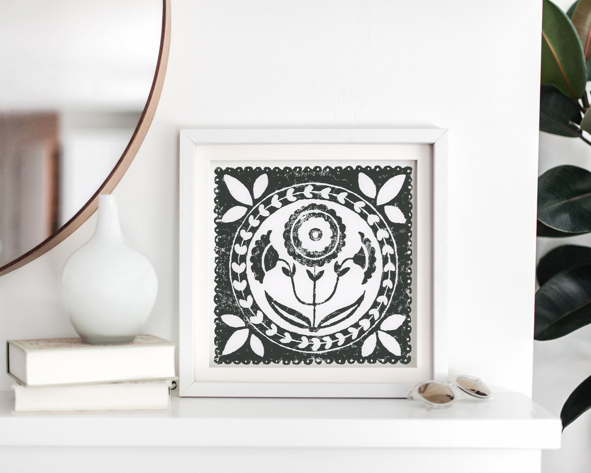 Framed black and white artwork on a shelf with books and a vase.