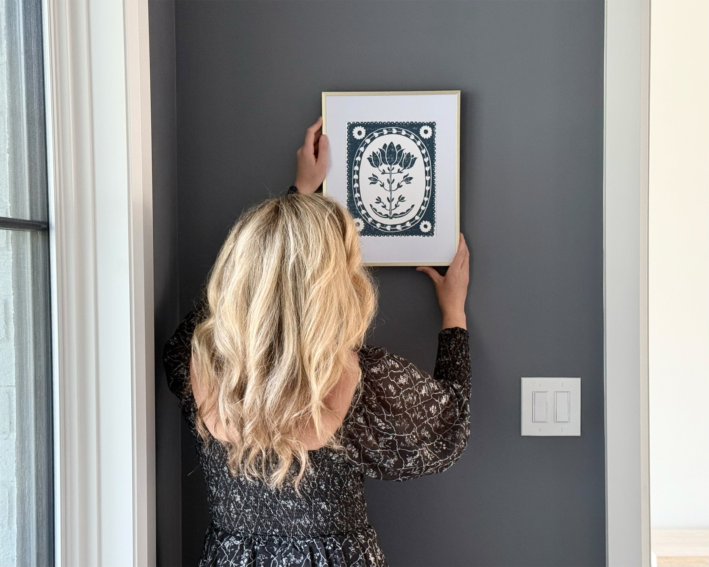 Woman hanging a framed picture on a gray wall