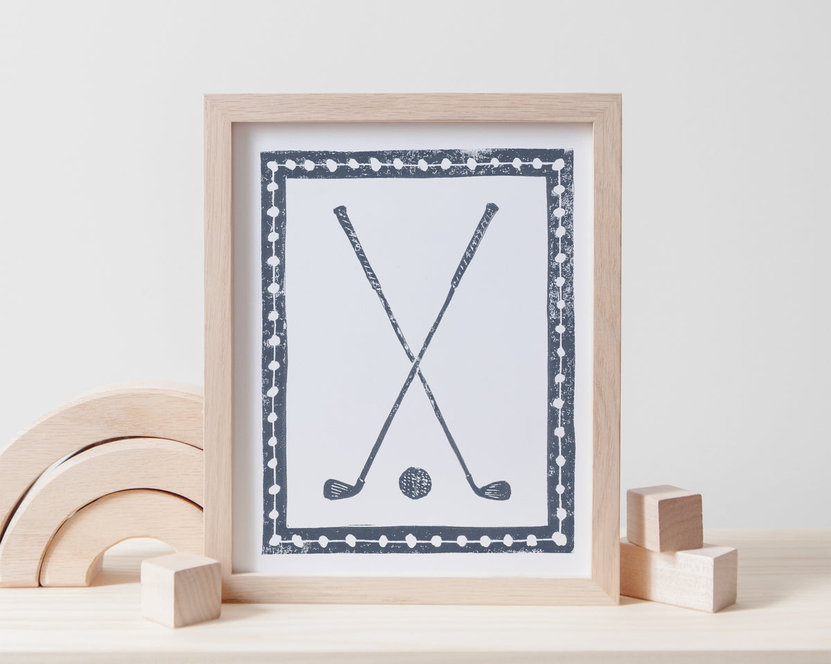 Framed artwork of crossed golf clubs and a golf ball on a white surface with wooden toys.