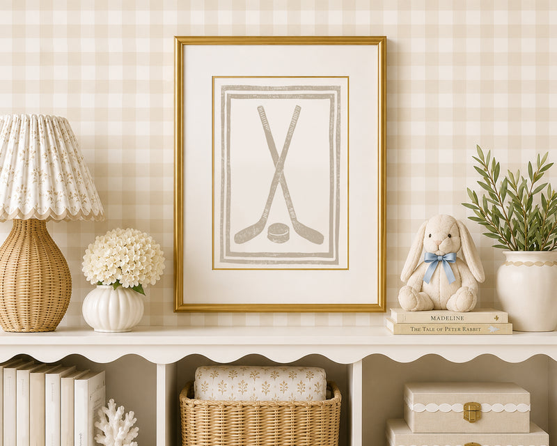 A sand tan and white hockey stick art print in a gold matted frame on a styled shelf in a tan and white bedroom