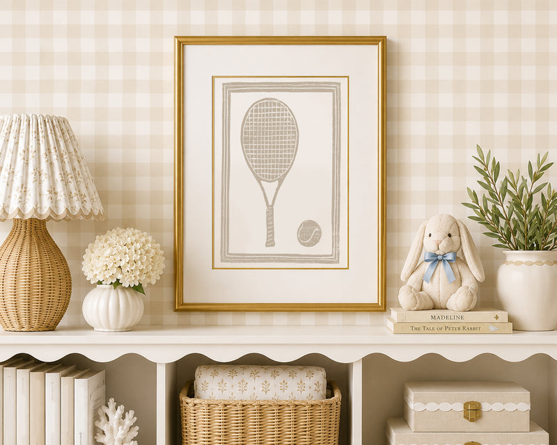 A sand tan and white tennis racket art print in a gold matted frame on a styled shelf in a tan and white bedroom