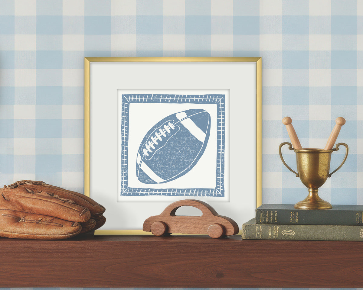 Framed artwork of a blue and white football on a white background, displayed on a shelf with a checkered wall.