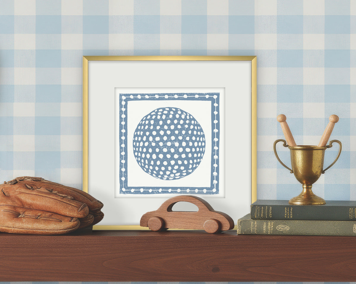Framed artwork of a blue and white golf ball on a white background, displayed on a shelf with a checkered wall.