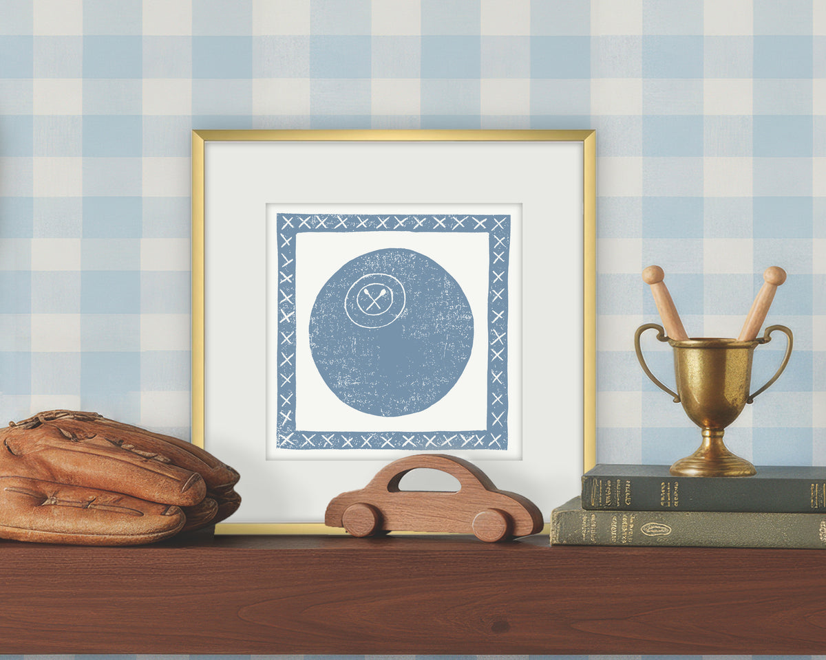 Framed artwork of a blue and white lacrosse ball on a white background, displayed on a shelf with a checkered wall.