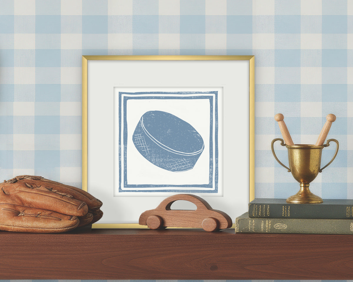 Framed artwork of a blue and white hockey puck on a white background, displayed on a shelf with a checkered wall.