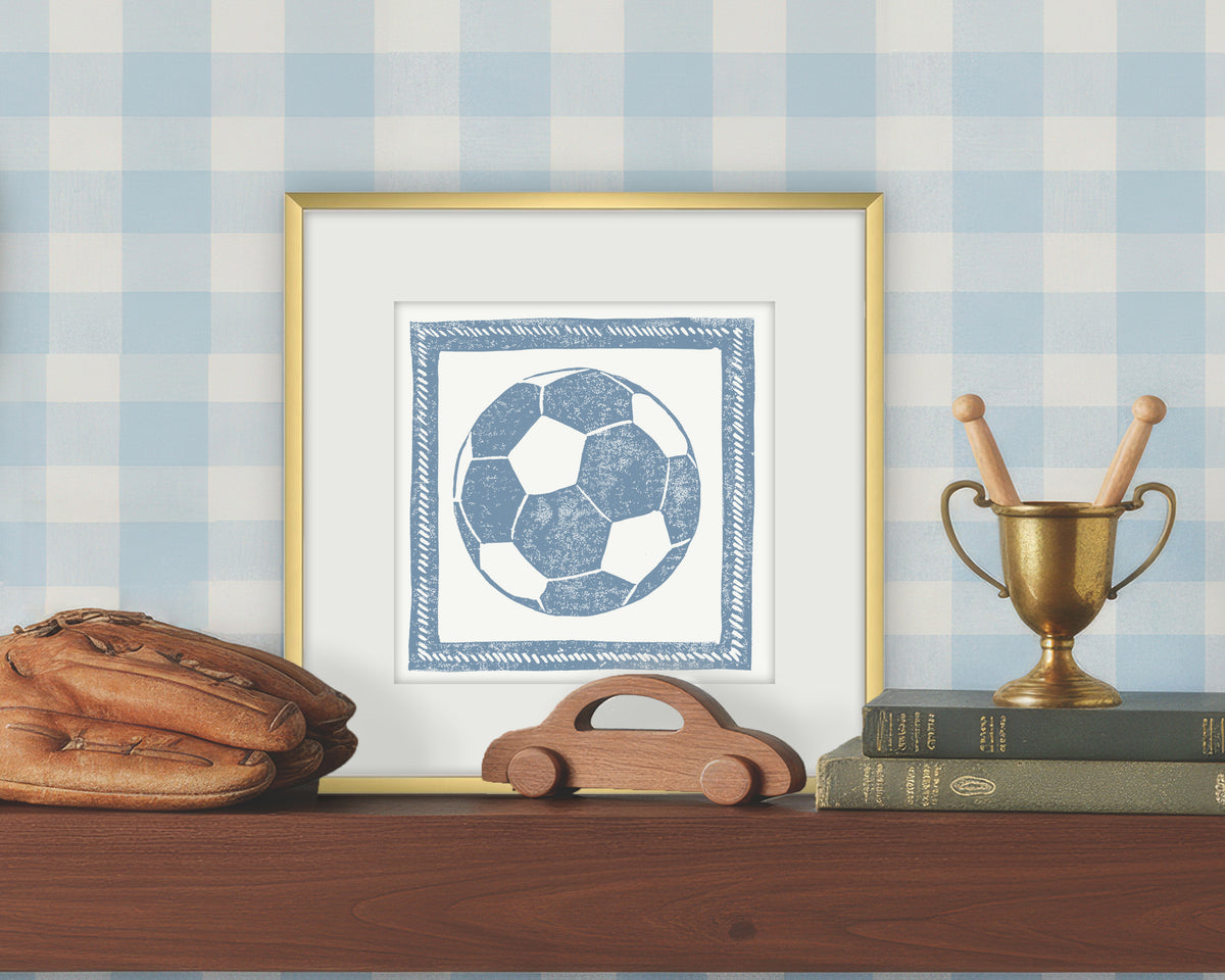 Framed artwork of a blue and white soccer ball on a white background, displayed on a shelf with a checkered wall.