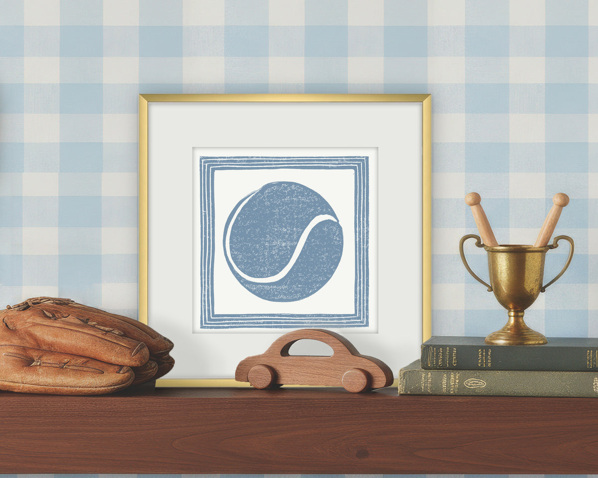 Framed artwork of a blue and white tennis ball on a white background, displayed on a shelf with a checkered wall.