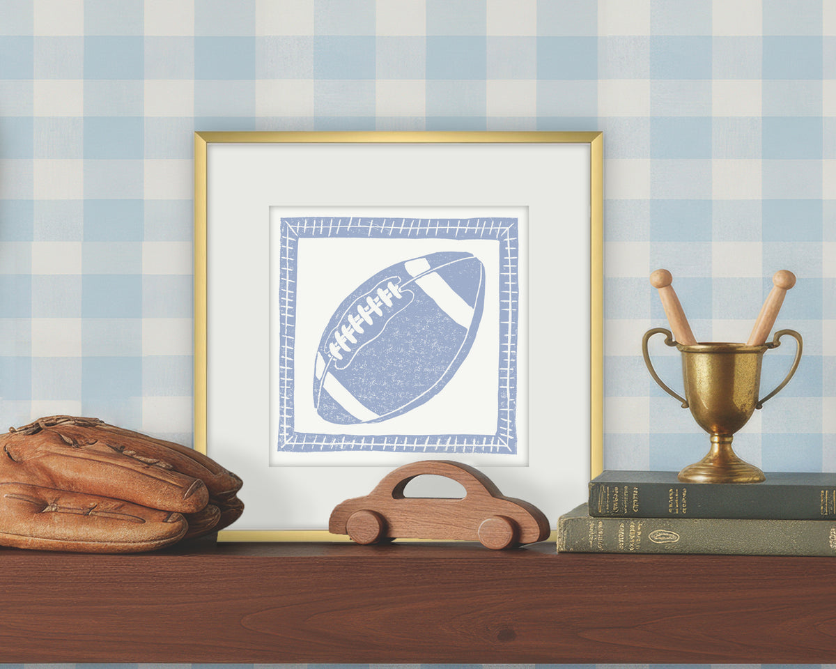 Framed artwork of a blue and white football on a white background, displayed on a shelf with a checkered wall.