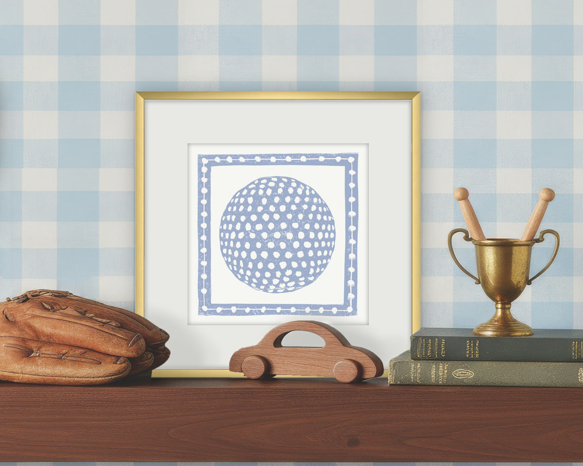 Framed artwork of a blue and white golf ball on a white background, displayed on a shelf with a checkered wall.