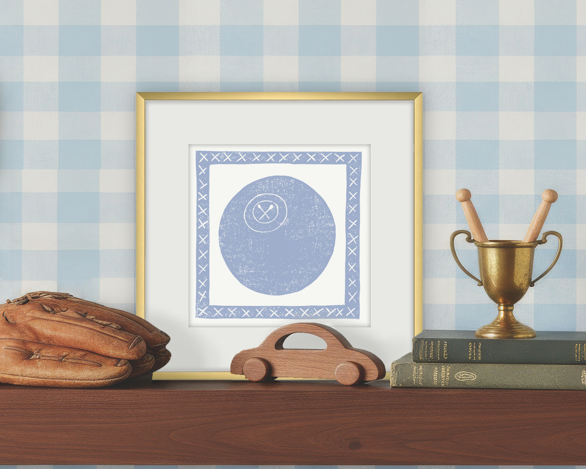 Framed artwork of a blue and white volleyball on a white background, displayed on a shelf with a checkered wall.