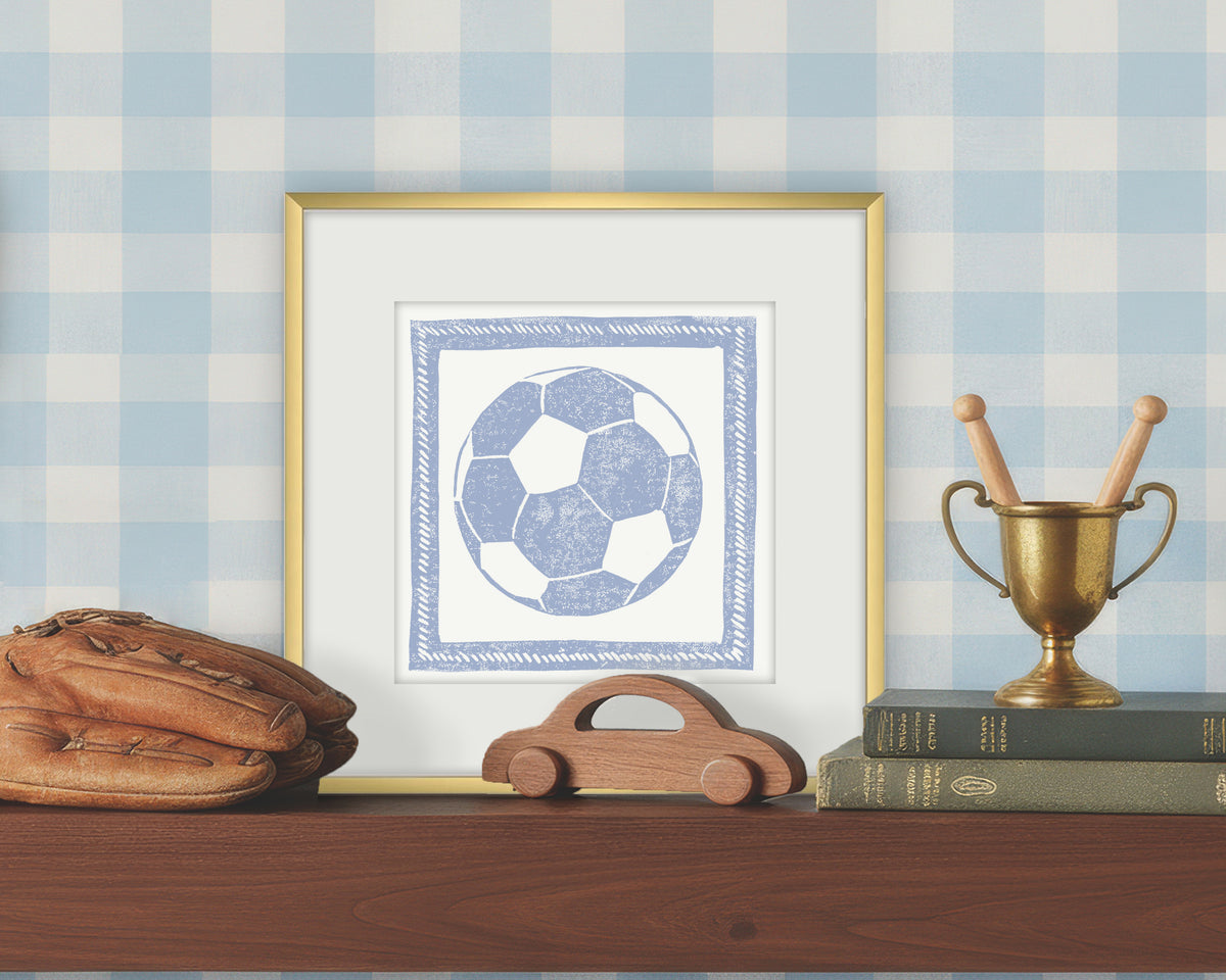 Framed artwork of a blue and white soccer ball on a white background, displayed on a shelf with a checkered wall.