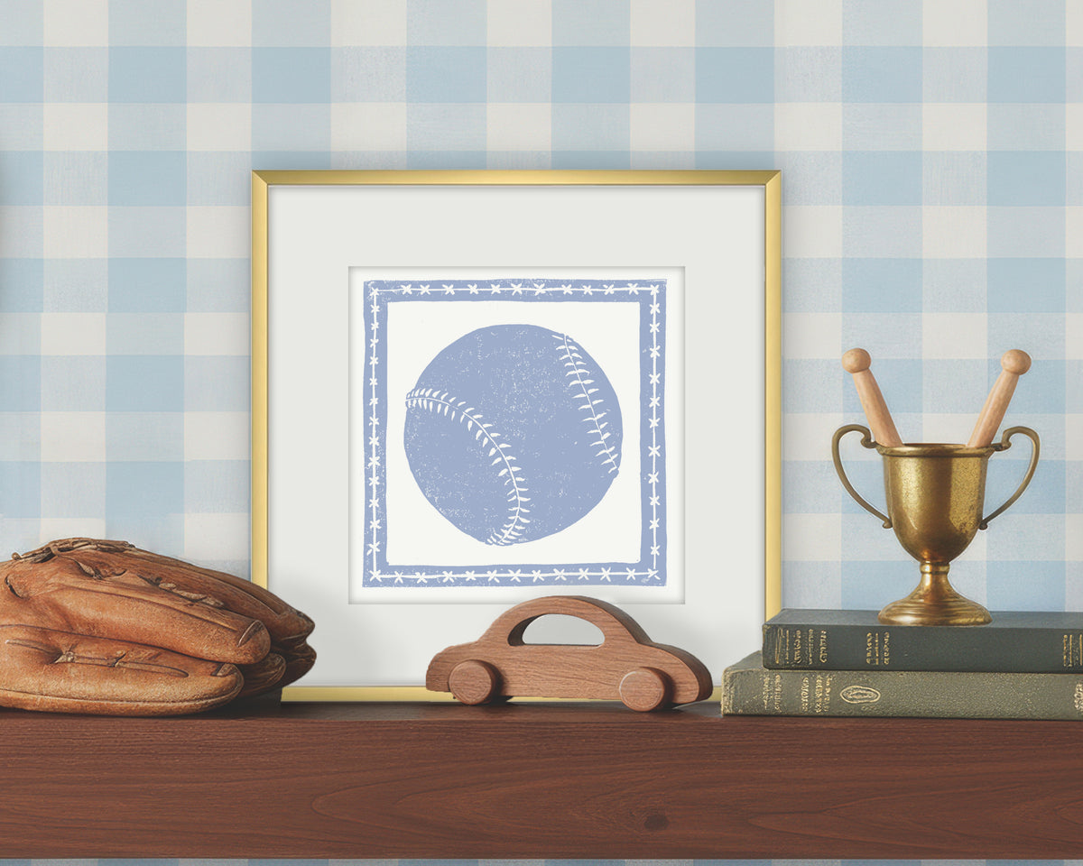 Framed artwork of a blue and white softball or baseball on a white background, displayed on a shelf with a checkered wall.