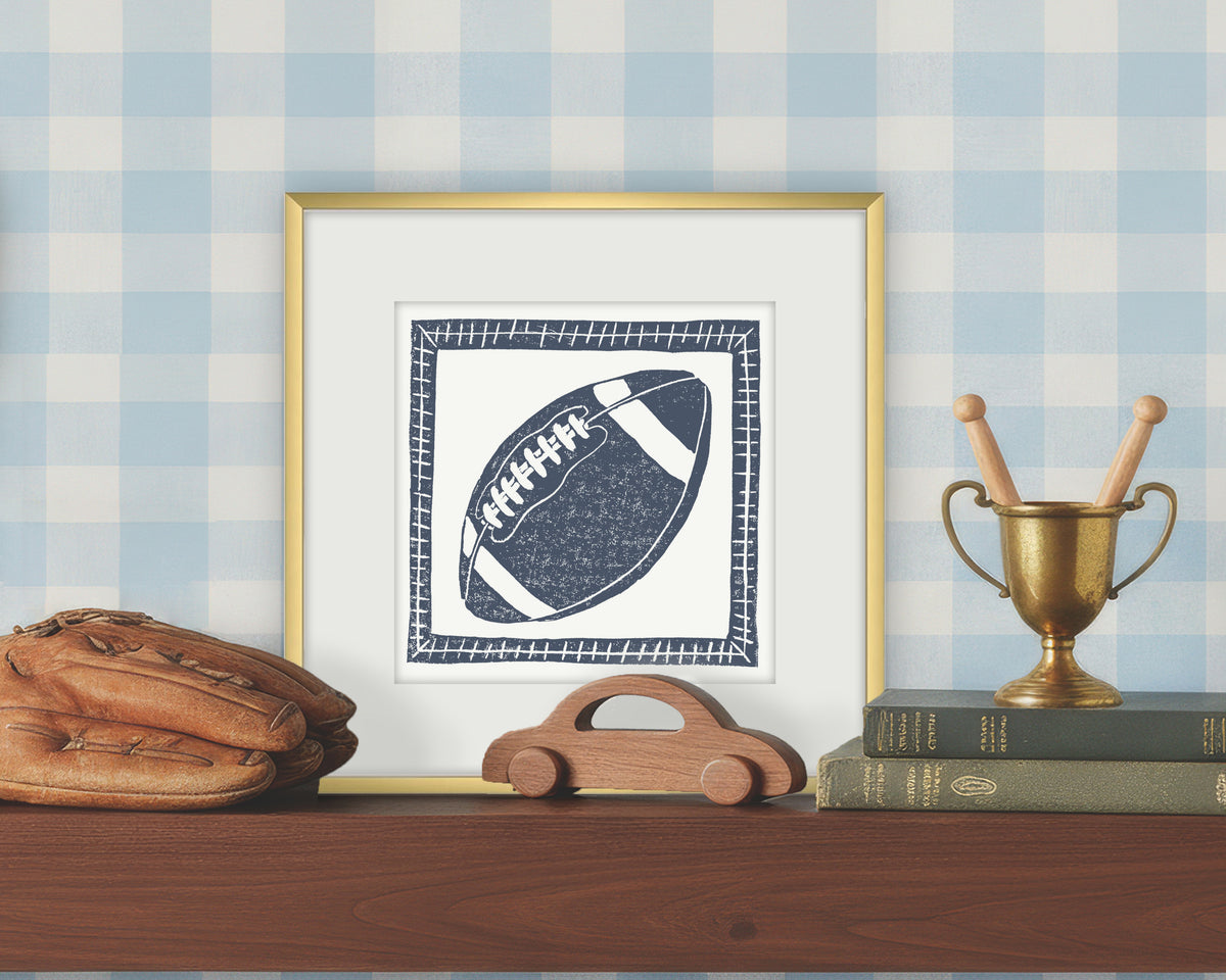 Framed artwork of a blue and white football on a white background, displayed on a shelf with a checkered wall.