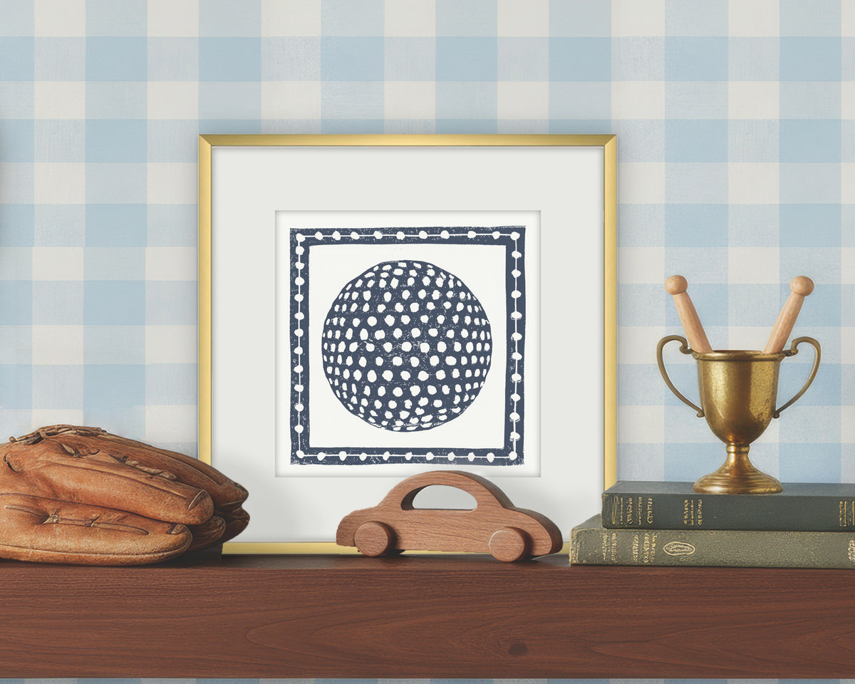 Framed artwork of a blue and white golf ball on a white background, displayed on a shelf with a checkered wall.